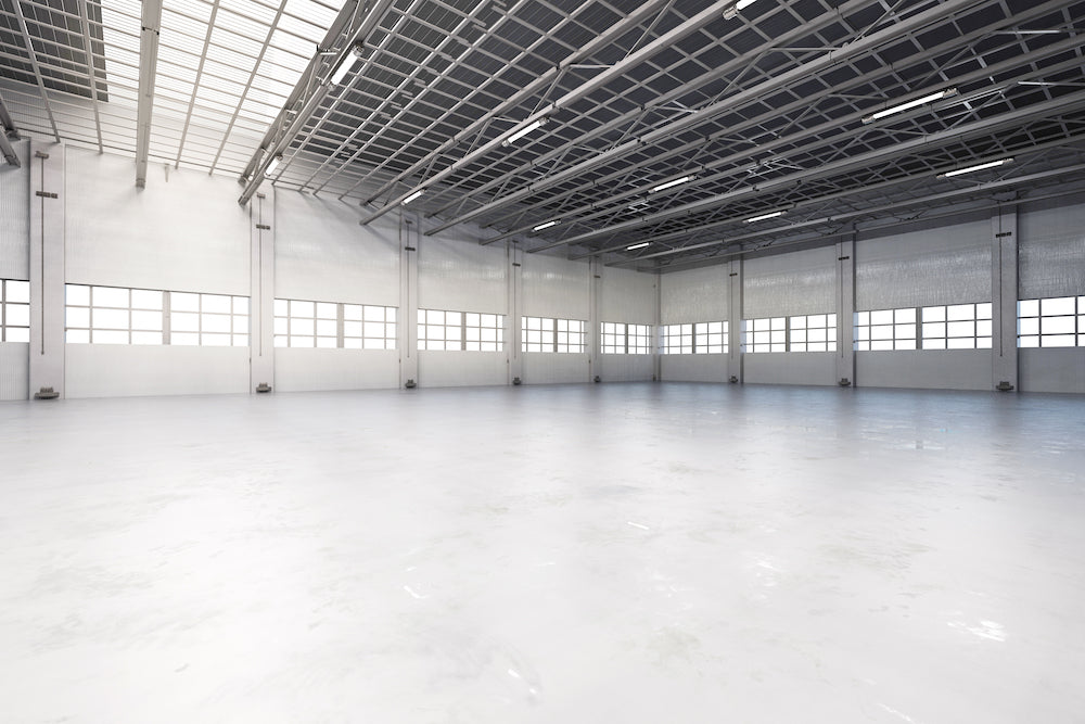 A large industrial warehouse space with a minimal epoxy resin polished concrete grind and seal project installed with a white metallic design.