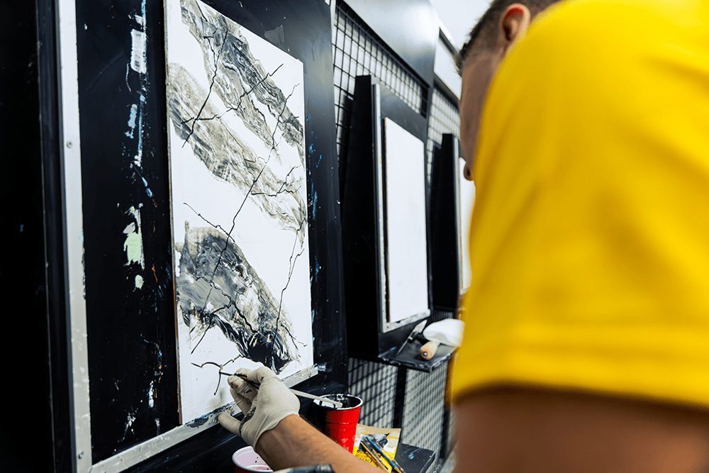 A man in a yellow shirt practicing Venetian wall art on a sample board.
