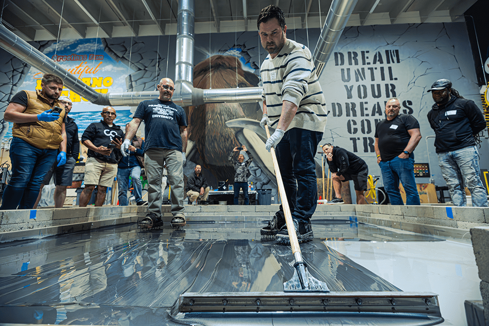 A man pushing a squeegee across an epoxy floor with people standing in the background.